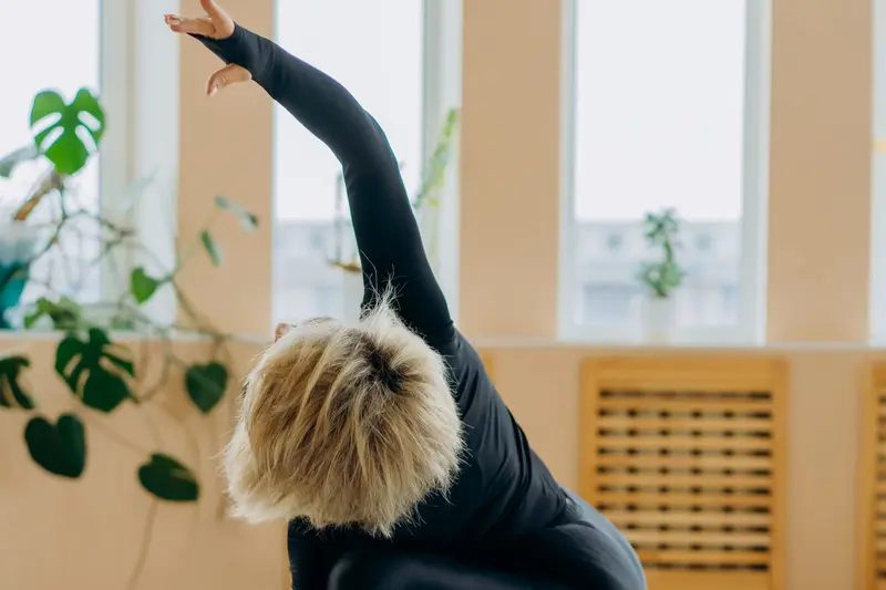 An older woman stretches on a yoga mat in a sunny living room